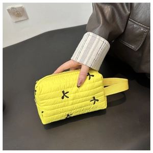 Detail of yellow quilted makeup bag featuring black bow embroidery and fabric handle