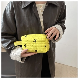 Close-up of bright yellow quilted handbag with black bow patterns and top handle detail