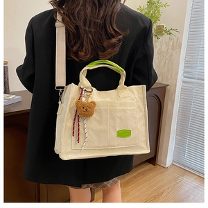 Detail of cream corduroy tote bag featuring a green patch and plush bear charm