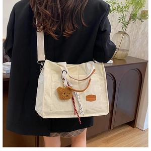 Detail of off-white corduroy tote bag with brown leather handles and cute bear charm