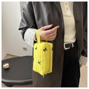 Detail of yellow quilted makeup bag with black bow embroidery and fabric handle