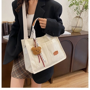 Detail of cream corduroy tote bag with bear charm and brown leather handle