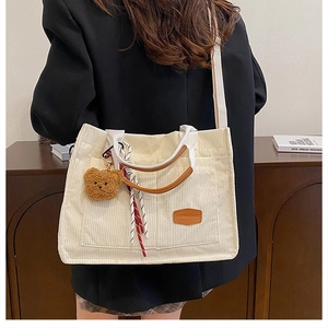 Detail of white corduroy tote bag with bear charm and contrast brown leather handles