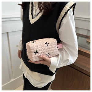 Detail view of pink quilted cosmetic bag with black embroidered bows and top handle