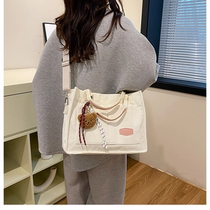 Detailed texture of white corduroy tote bag with brown plush bear charm and pink label