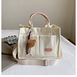 Detail of corduroy tote bag with pink leather handles and cute brown bear pendant