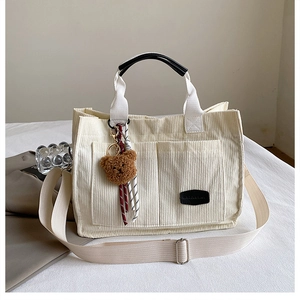 Detail of corduroy tote bag featuring front pockets and brown plush bear charm accessory