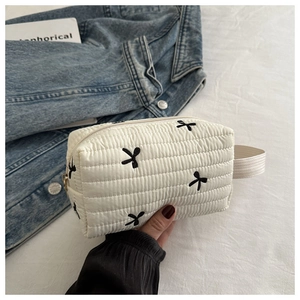 Close-up of white quilted cosmetic bag featuring black embroidered bow details and zip handle