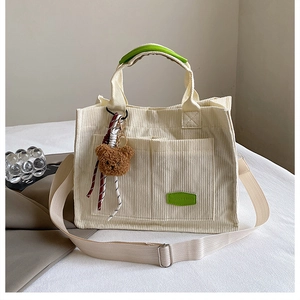 Detail of cream corduroy tote bag with dual front pockets and brown plush bear charm