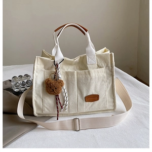 Detail of cream corduroy tote bag with brown leather handles and plush bear charm