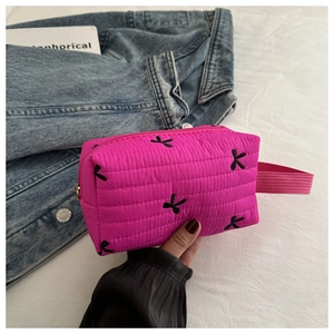 Close-up of rose pink quilted makeup bag with black floral embroidery and zipper detail