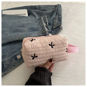 Close-up of pink quilted cosmetic bag with black bow embroidery and gold zipper detail