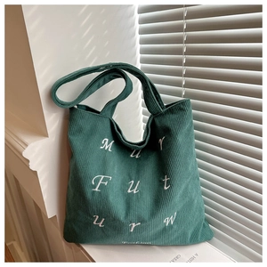 Close-up of green corduroy tote bag featuring white letter embroidery and soft texture