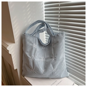 Close-up of light blue corduroy tote bag showing high-quality letter embroidery detail