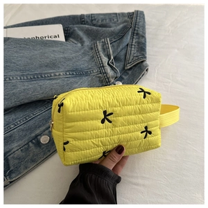 Detail of yellow quilted makeup bag with black bow embroidery and sturdy carry handle