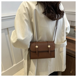 Détail d'un sac bandoulière en cuir marron avec boucle dorée sur un trench-coat beige