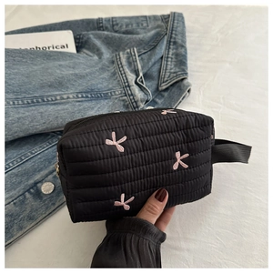 Close-up of black quilted makeup bag with pink embroidered bows and top handle