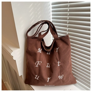 Close-up of brown corduroy tote bag featuring white embroidered letters on soft texture