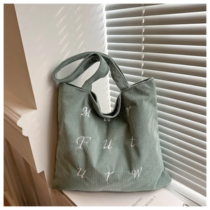 Detail of grey-green corduroy tote bag showing white embroidery and natural light texture