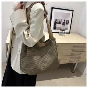 Détail d'un grand sac cabas tressé marron avec anse en cuir porté par un mannequin