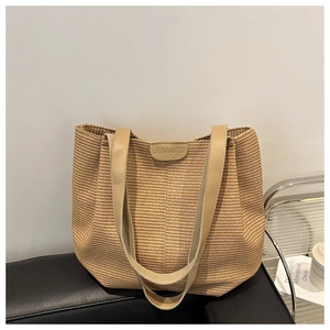 Gros plan du sac cabas en paille tissée avec anses en cuir marron et écusson de marque