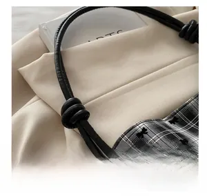 Detail of black and white plaid handbag featuring bow embroidery and leather rope strap