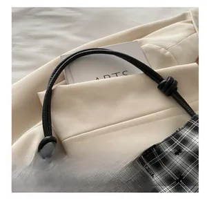 Detail of checkered bucket bag with bow embroidery and knotted black handle strap