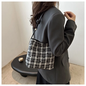 Detail of checkered shoulder bag with black bows and knotted strap craftsmanship