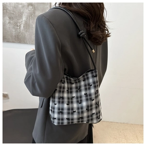 Detail of checkered shoulder bag with black bows and knotted leather strap on a model