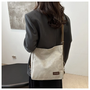 Detail of off-white denim tote bag with brown leather strap and front pocket
