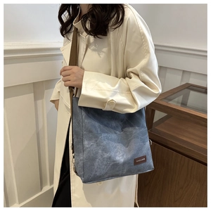 Denim blue crossbody bag with wash texture and brown fabric strap shown on model