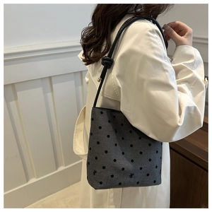 Detail of grey polka dot bucket bag with black rope strap on a model shoulder