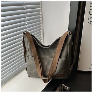 Detail of grey denim tote bag featuring dual front pockets and brown woven strap