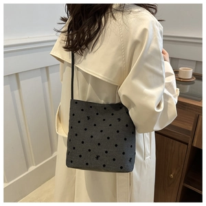 Detail view of grey polka dot canvas bucket bag with bow embroidery on a model