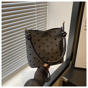 Close-up of gray bucket bag featuring black polka dots and embroidered bow details