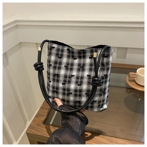 Detail of checkered bucket bag with black bow embroidery and metallic cord tips