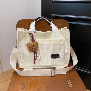 Chic corduroy tote bag in cream white with plush bear charm on a wooden chair