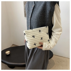 Detail of cream quilted makeup bag featuring black bow embroidery and soft striped texture