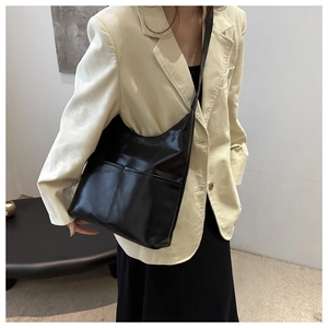 Detail of a black leather tote bag with functional front pockets and a glossy finish