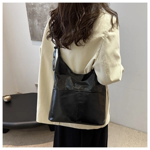 Close-up of black glossy leather tote bag with shoulder knot detail on model