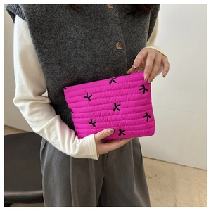 Detail view of a pink quilted cosmetic bag featuring black bow embroidery held by a model