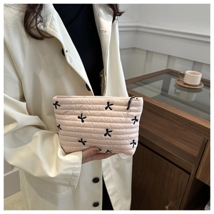 Detail of pink quilted makeup bag featuring black bow embroidery and secure zipper