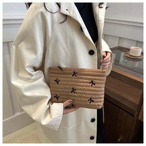 Detail of beige quilted clutch bag with floral embroidery held by a model in trench coat