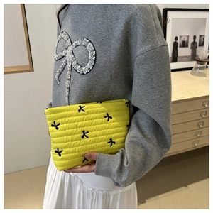 Detail view of quilted yellow clutch bag with black bow embroidery and textured horizontal seams