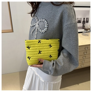 Quilted yellow makeup bag with black bow pattern held by a model in a lifestyle setting