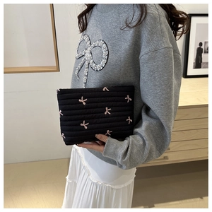 Detail of black quilted pouch with pink embroidered bows held against a neutral room