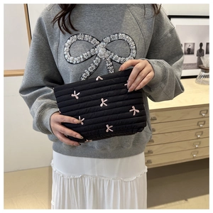 Handheld view of black quilted makeup bag with pink embroidered bow details