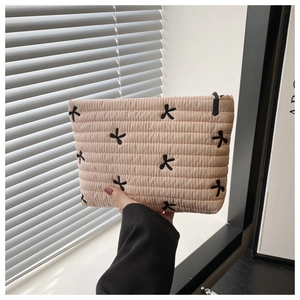 Detailed view of apricot quilted makeup bag featuring black embroidered bows and top zipper