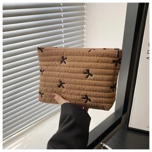 Close-up of khaki quilted cosmetic bag featuring embroidered black bows and zipper