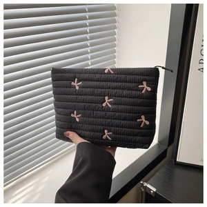 Close-up of black quilted clutch with pink bow embroidery held in hand indoors